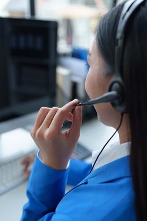 A call center agent wearing a headset provides customer service at a computer.