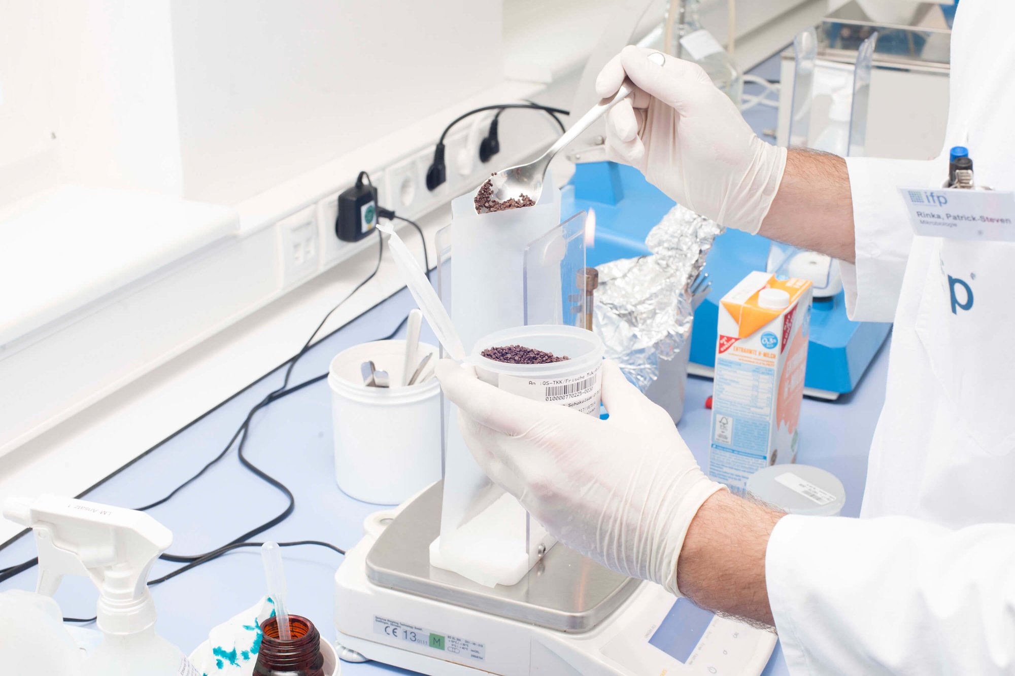 Scientist weighing granular sample material on a laboratory scale.