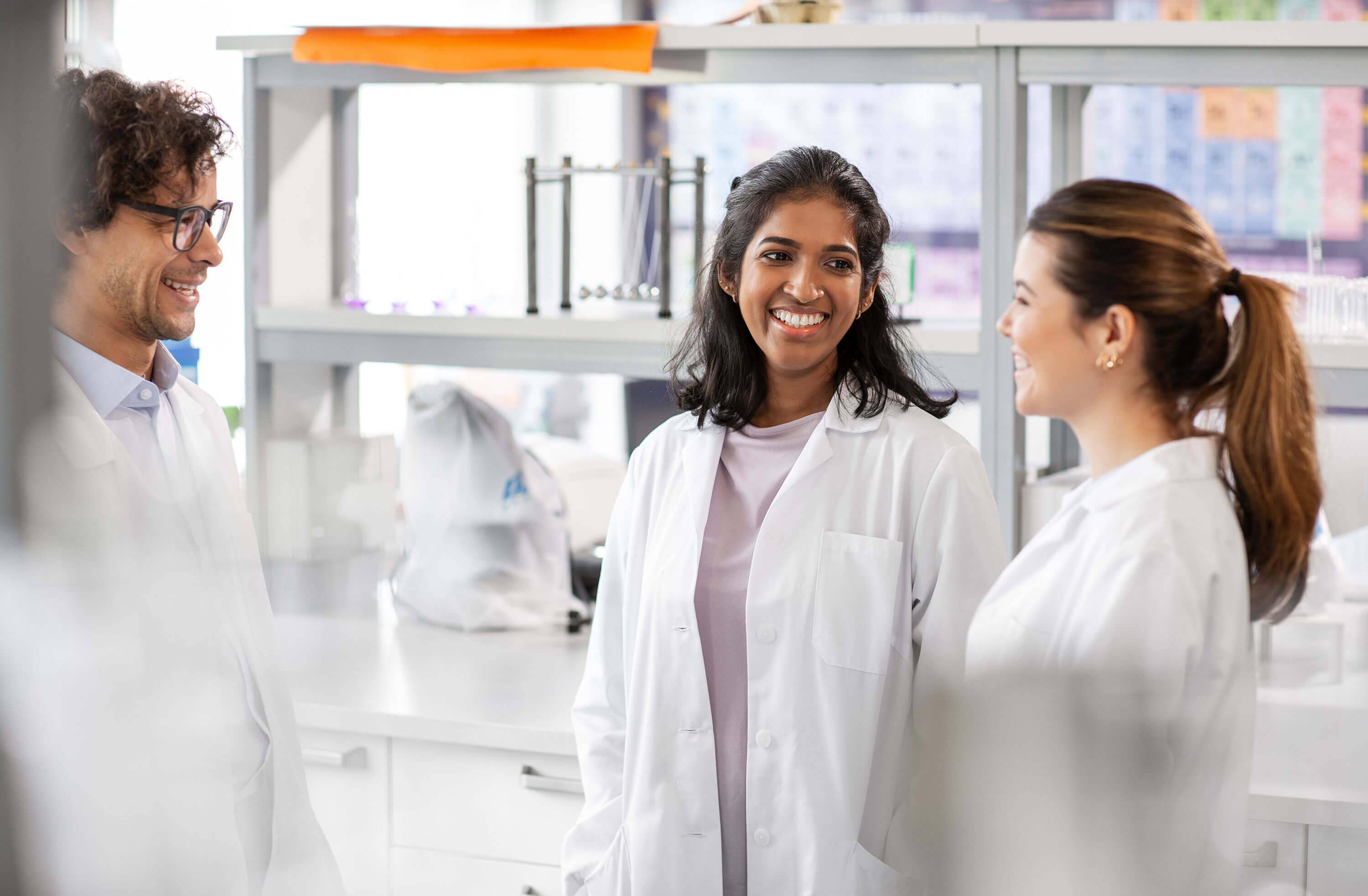 Three smiling scientists talk together in a laboratory.