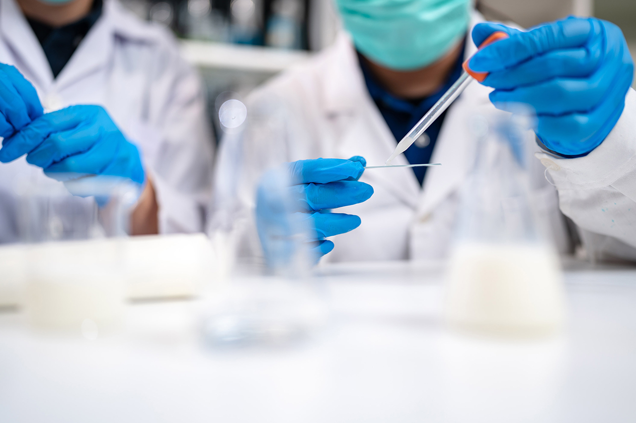 Two people wearing lab coats and gloves are engaged in a scientific task together in a laboratory environment.