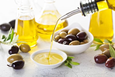 Close-up of olive oil pouring into a dish with green and black olives.