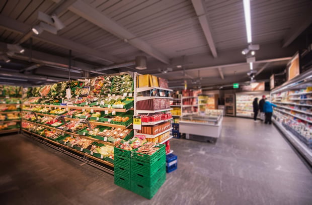 People shop in a modern supermarket with the vegetable section visible in the foreground.