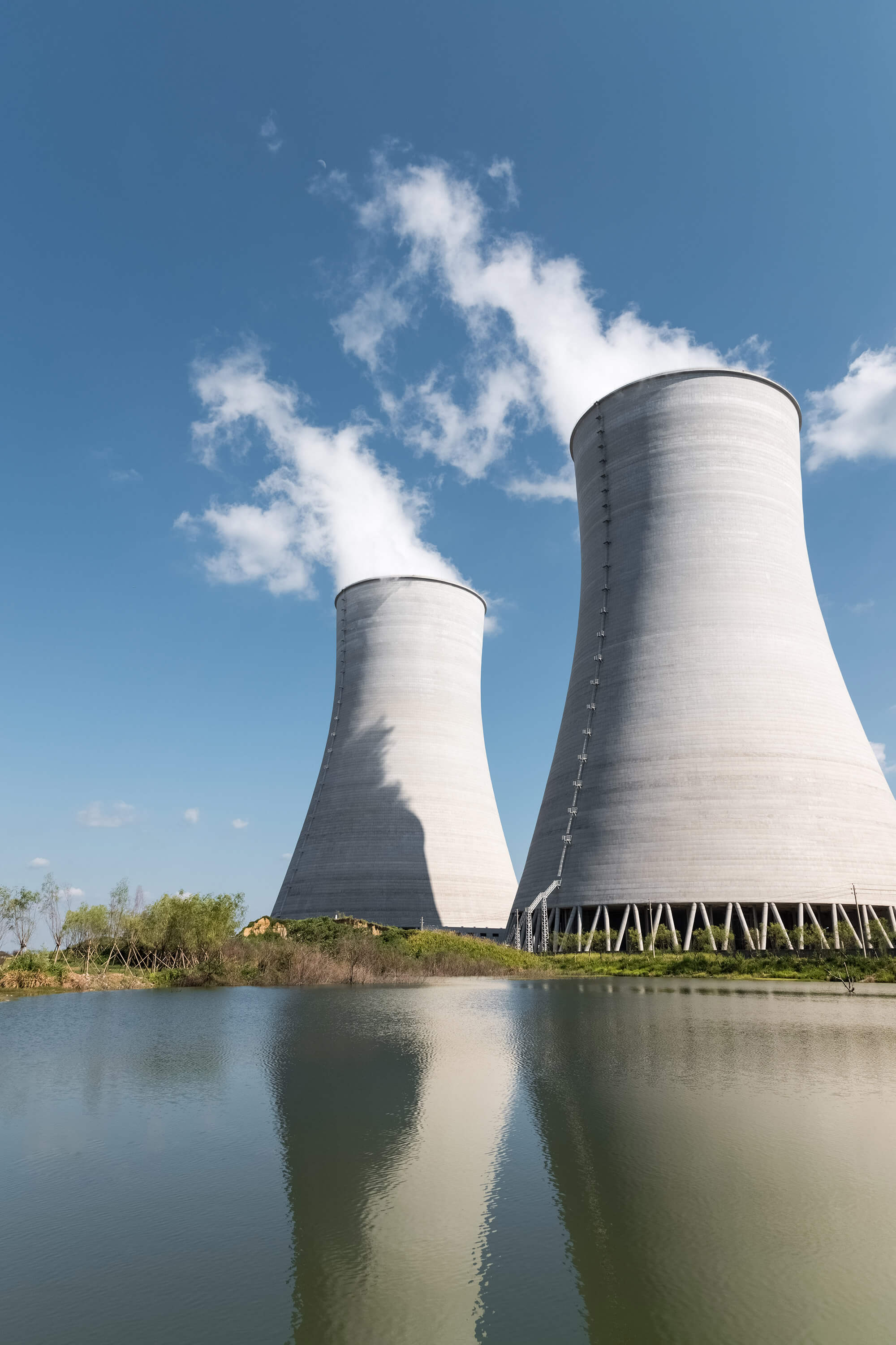 Two industrial cooling towers stand against a blue sky.