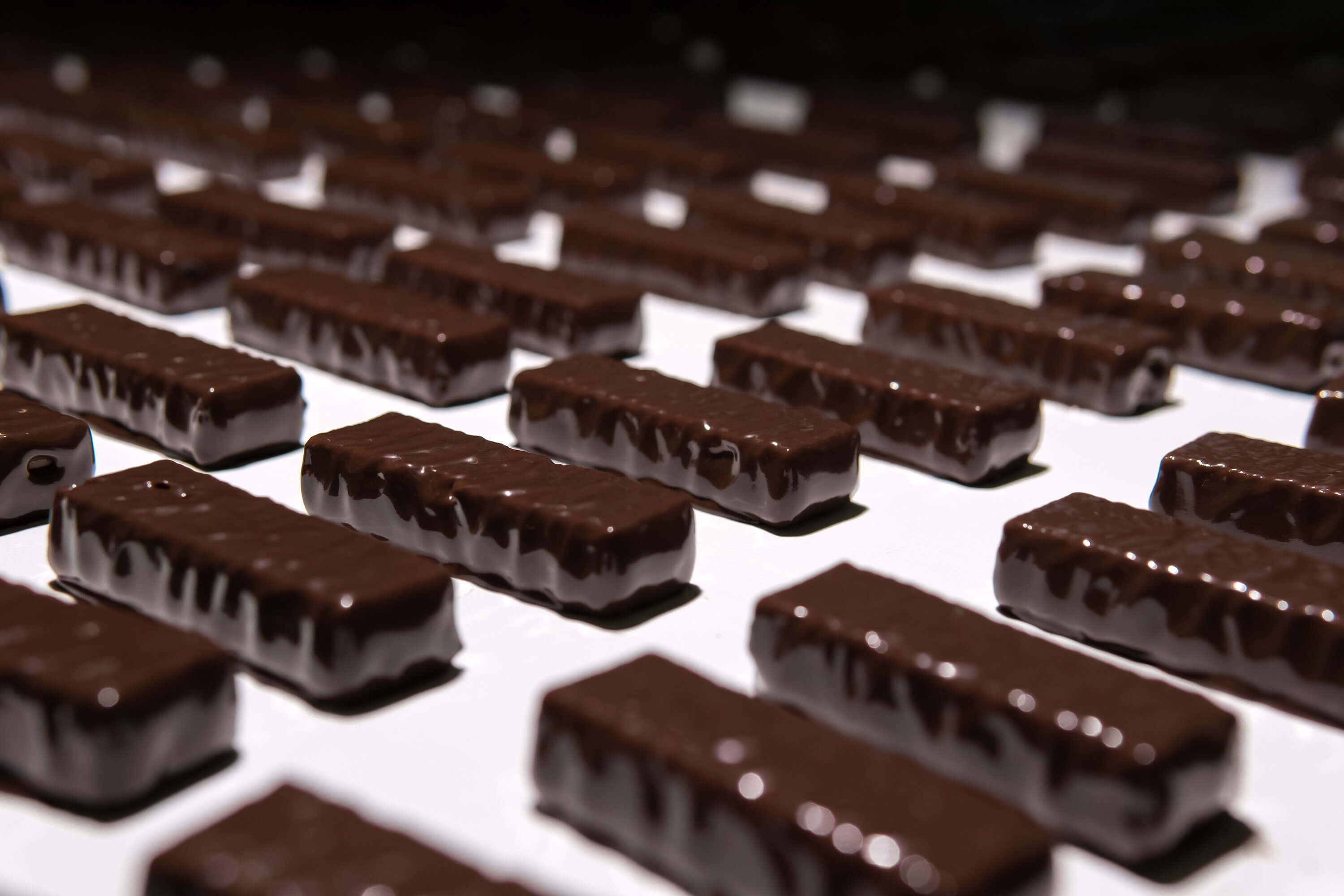 Close-up of chocolate candies moving along a conveyor belt in a confectionery factory.