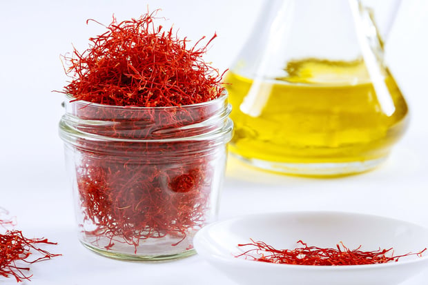 Dried saffron threads in a glass bottle and saffron extract are arranged on a white background.