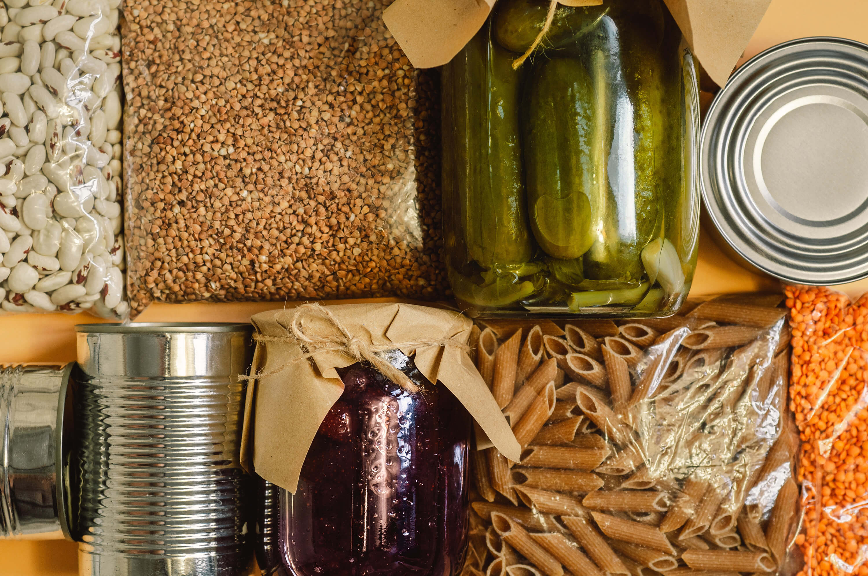 Food supplies including buckwheat, pasta, canned food, and lentils are arranged as a stock of essential goods.