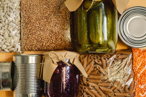 Food supplies including buckwheat, pasta, canned food, and lentils are arranged as a stock of essential goods.