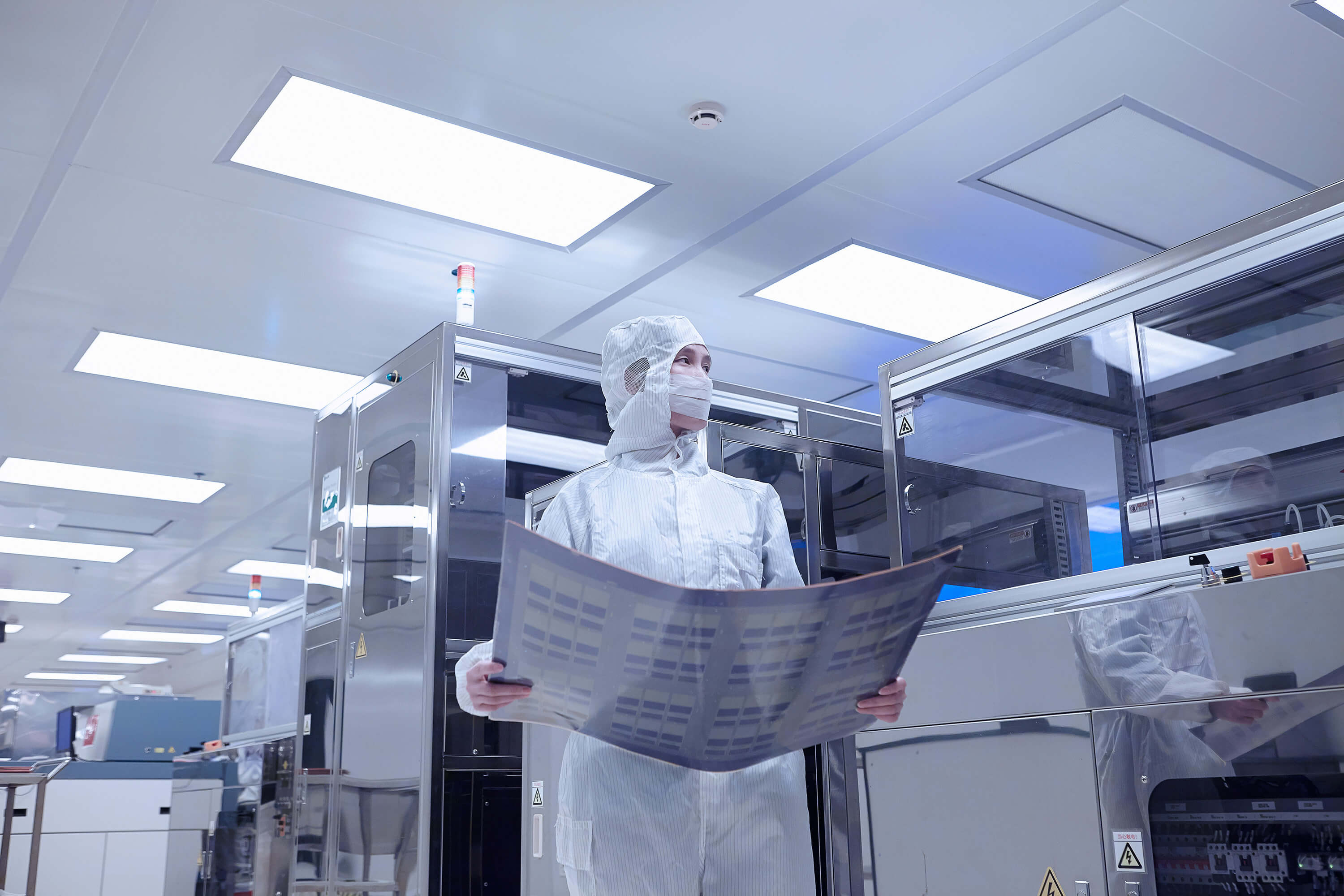 A worker holds a flexible circuit inside a clean room at an electronics factory.