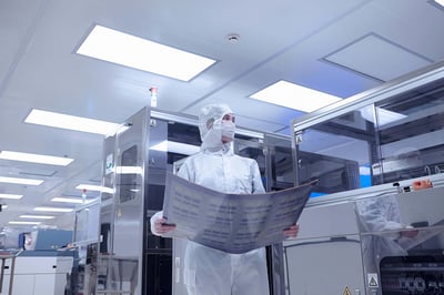 A worker holds a flexible circuit inside a clean room at an electronics factory.