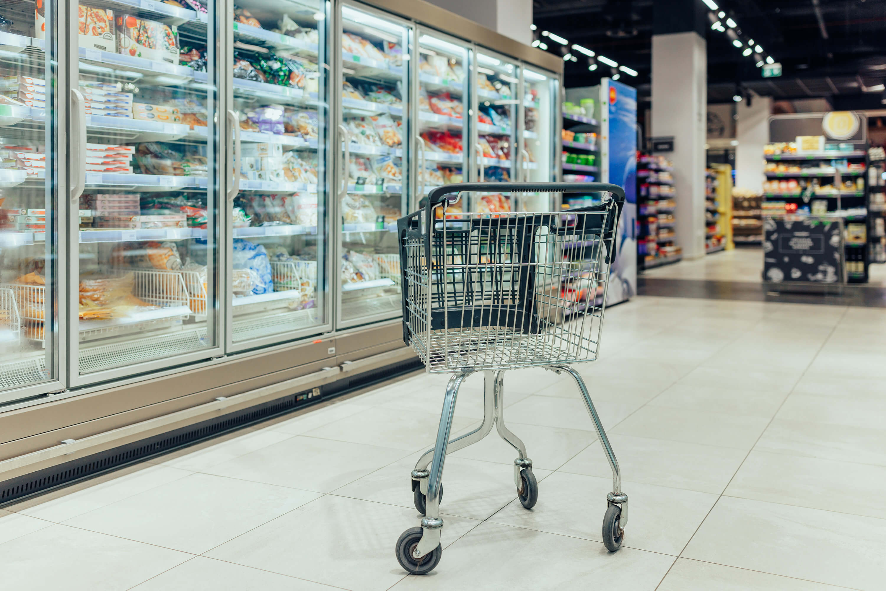 A shopping cart stands in a supermarket aisle with no people visible.