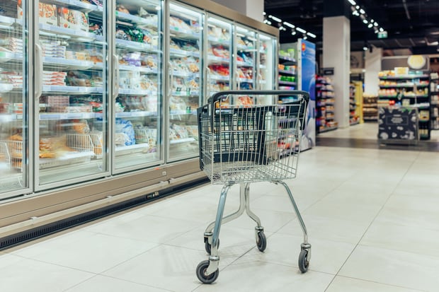 A shopping cart stands in a supermarket aisle with no people visible.