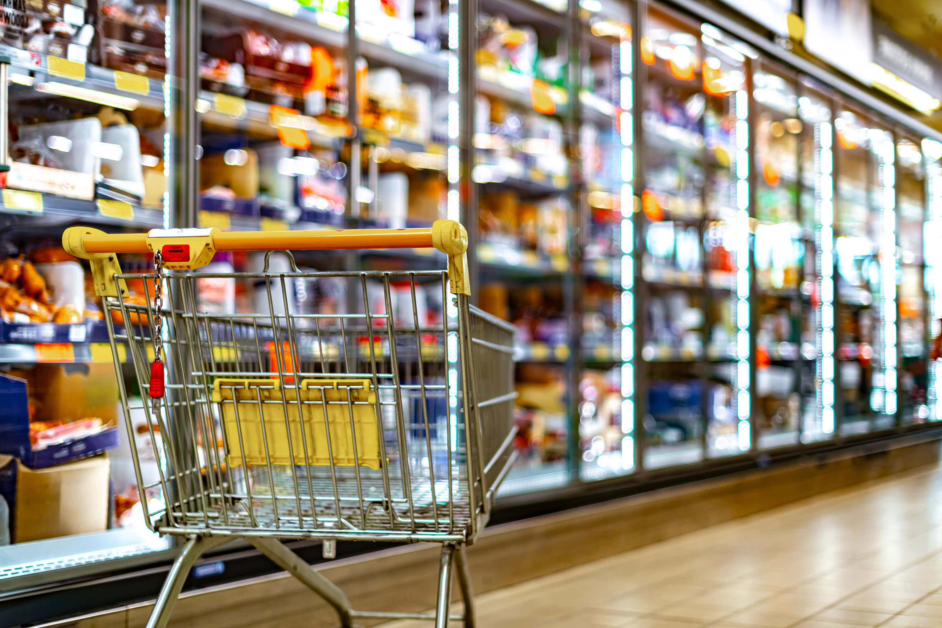 A shopping cart stands in front of store shelves in a supermarket.