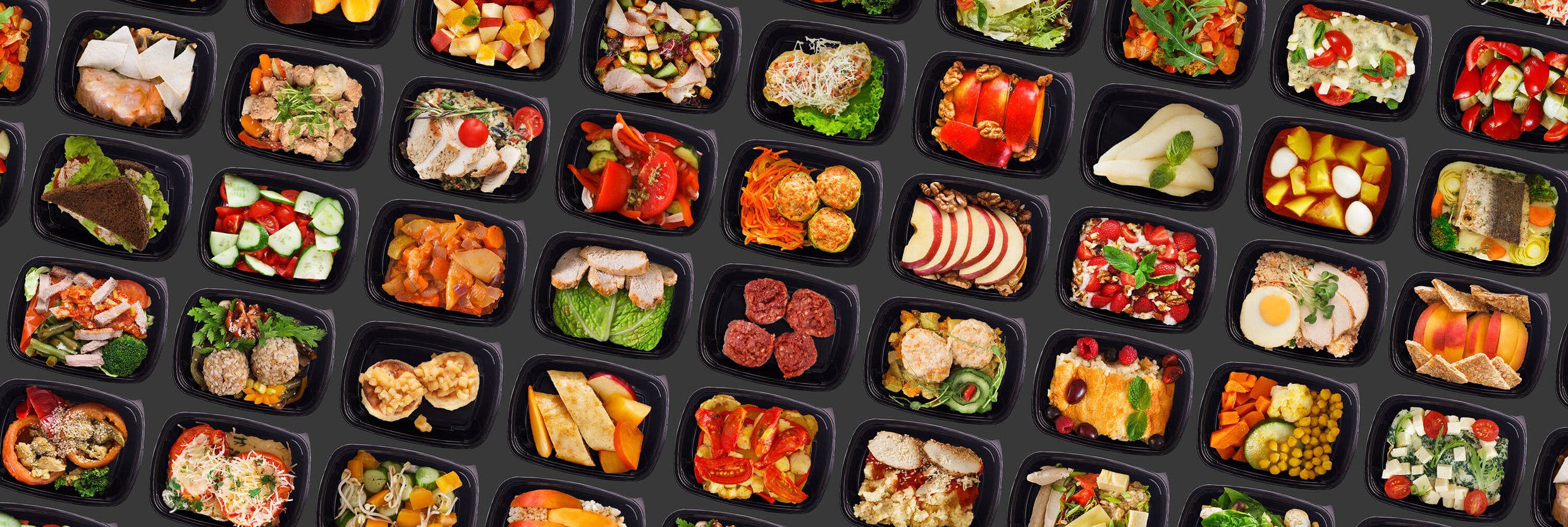 Take-away lunch boxes filled with prepared healthy meals on a black background.