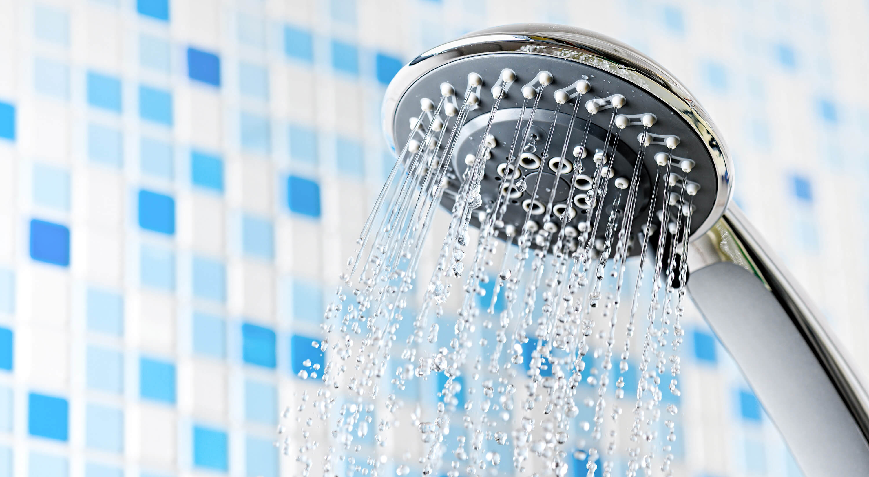 Shower head with running water in blue bathroom.