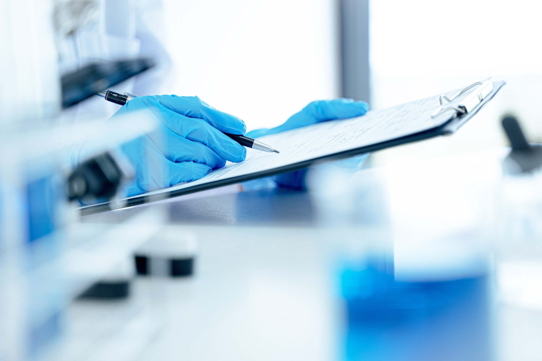 Scientist wearing gloves documenting laboratory results on a clipboard.
