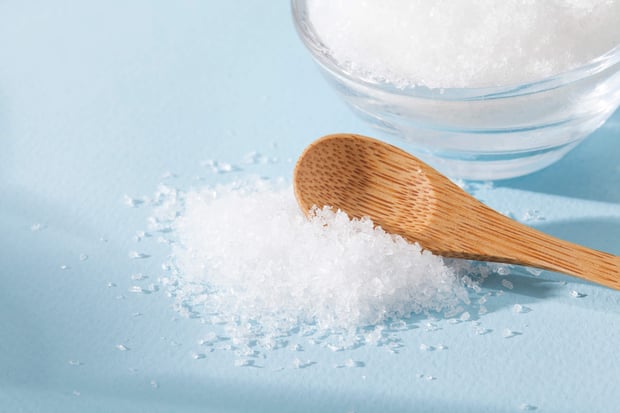 Magnesium chloride crystals with a wooden spoon and glass bowl on a light blue surface.