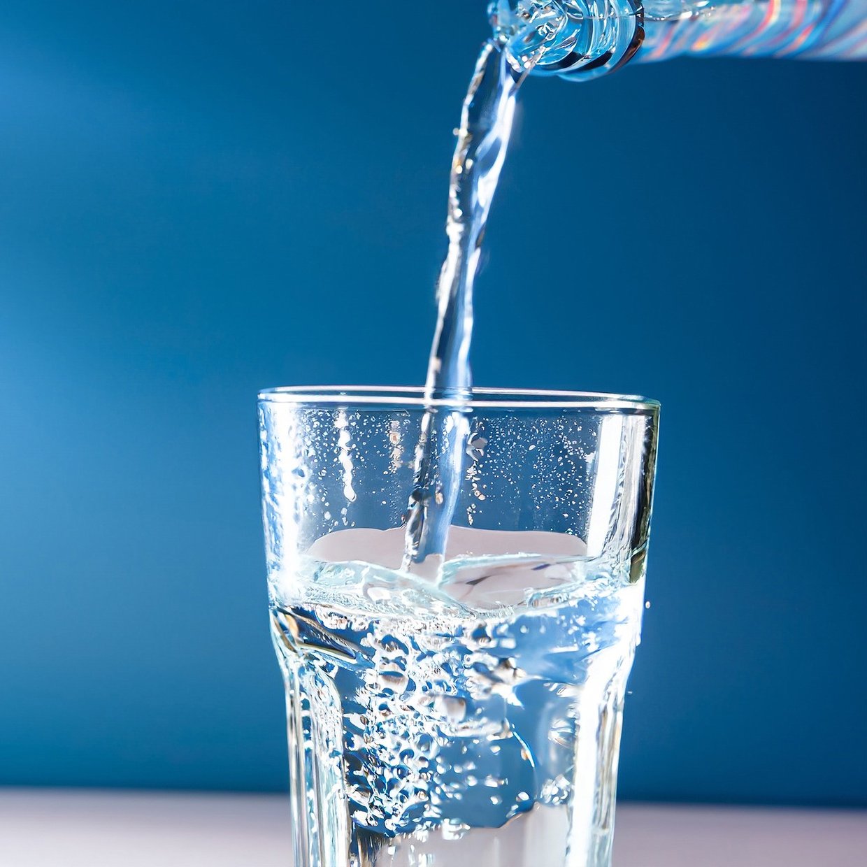 Carbonated mineral water being poured into a glass against a bright blue background.