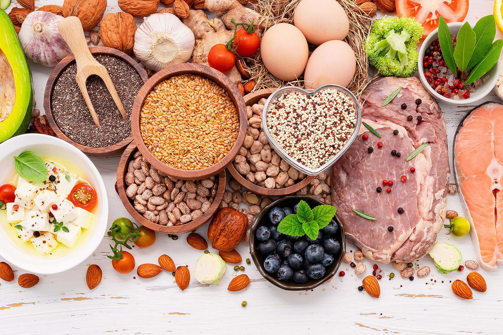 A selection of healthy ketogenic low-carb diet ingredients is arranged on a white wooden background.