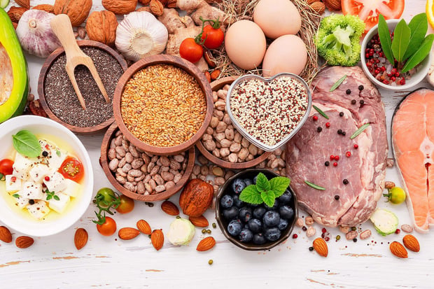 A selection of healthy ketogenic low-carb diet ingredients is arranged on a white wooden background.