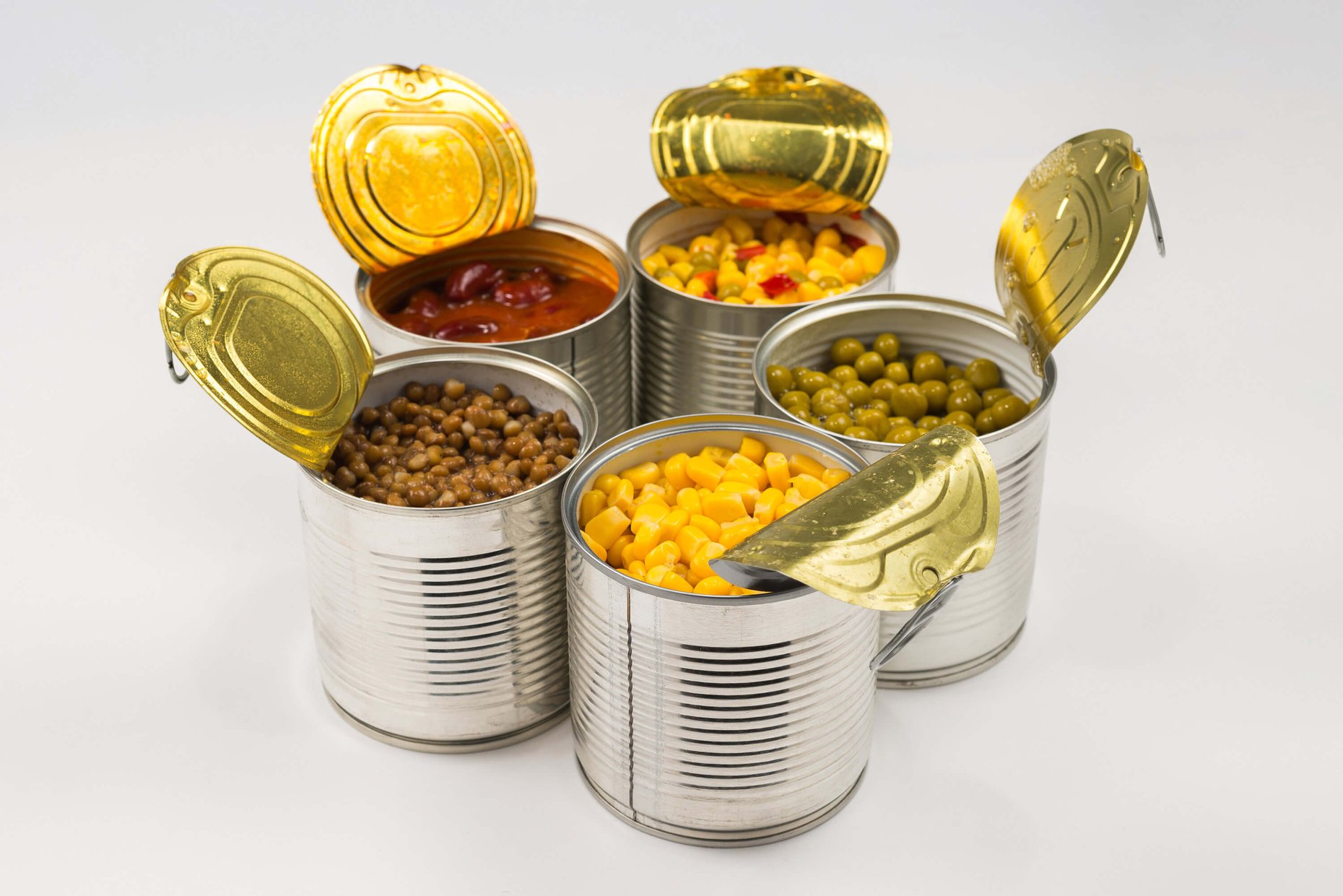 Canned food including green peas, beans, corn, and lentils arranged on a white background.