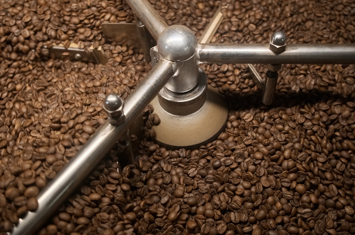 Roasted coffee beans in an industrial roaster cooling tray during processing.