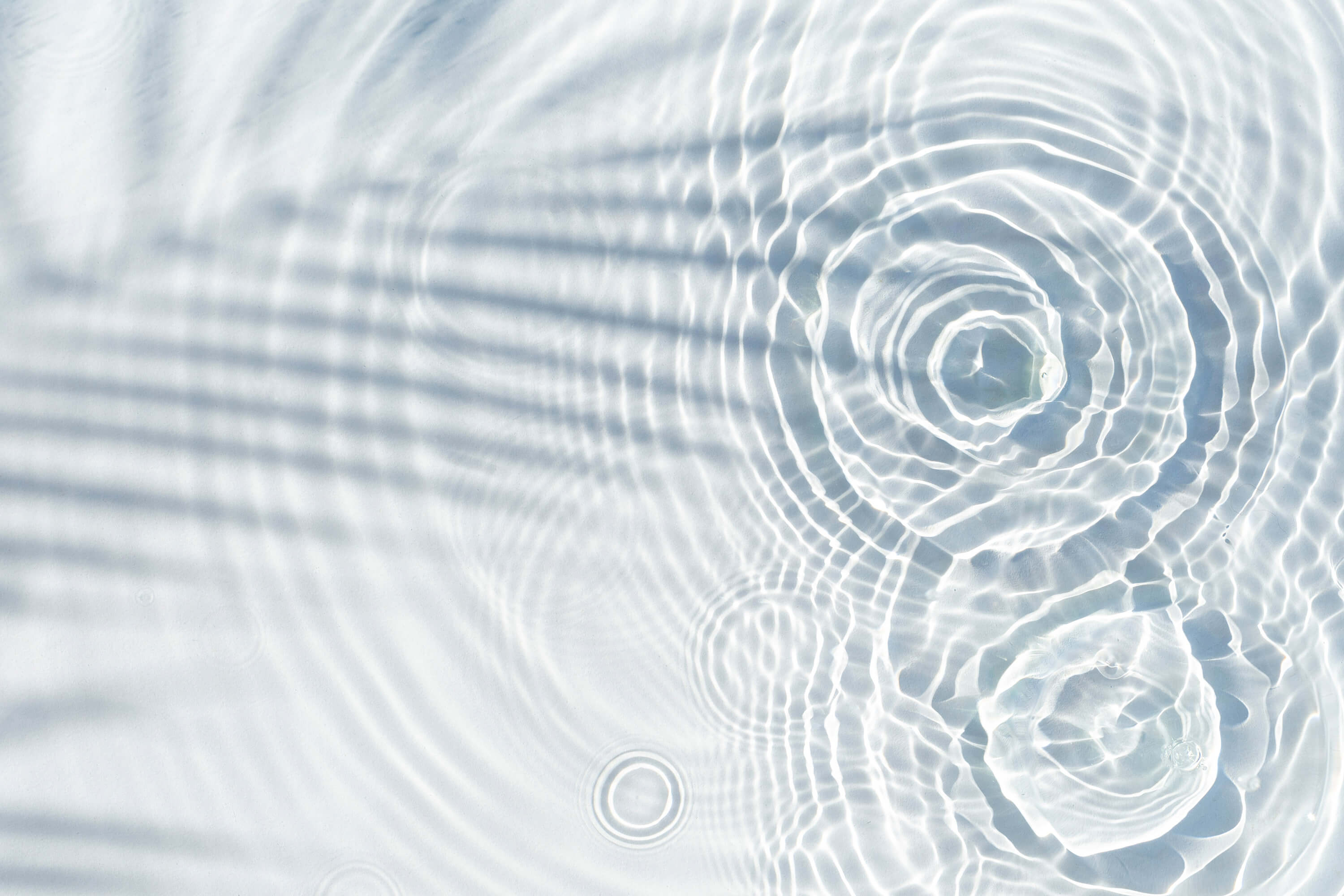 Water drops fall onto a transparent water surface, with the shadow of a palm leaf creating a flat-lay top view composition.