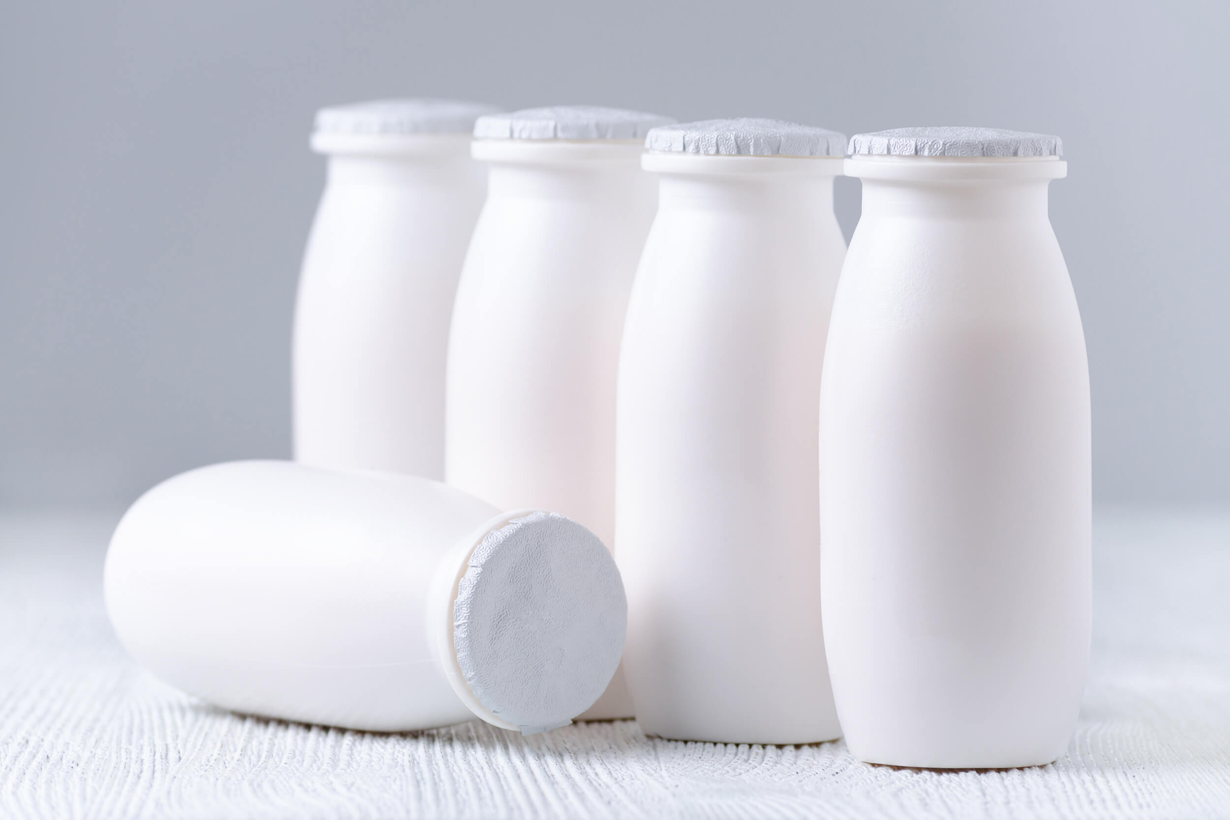 Several white yogurt bottles with sealed lids stand on a light-colored surface.
