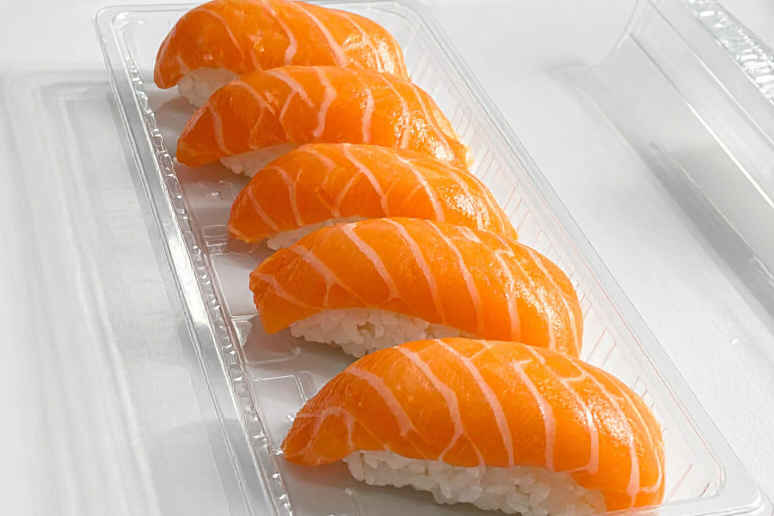 Several packages of sushi, including salmon and shrimp nigiri, are arranged on a white work surface.