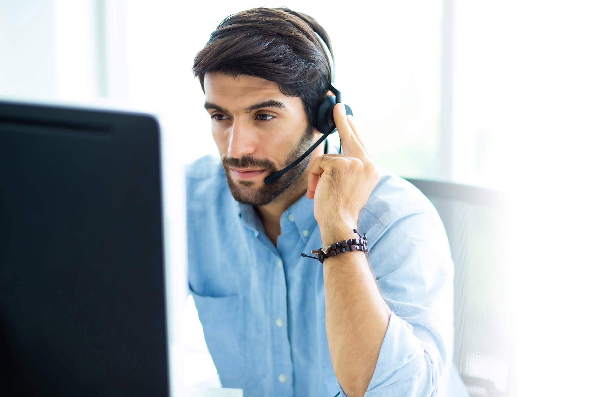 A male customer service representative wearing a headset speaks in a modern office.