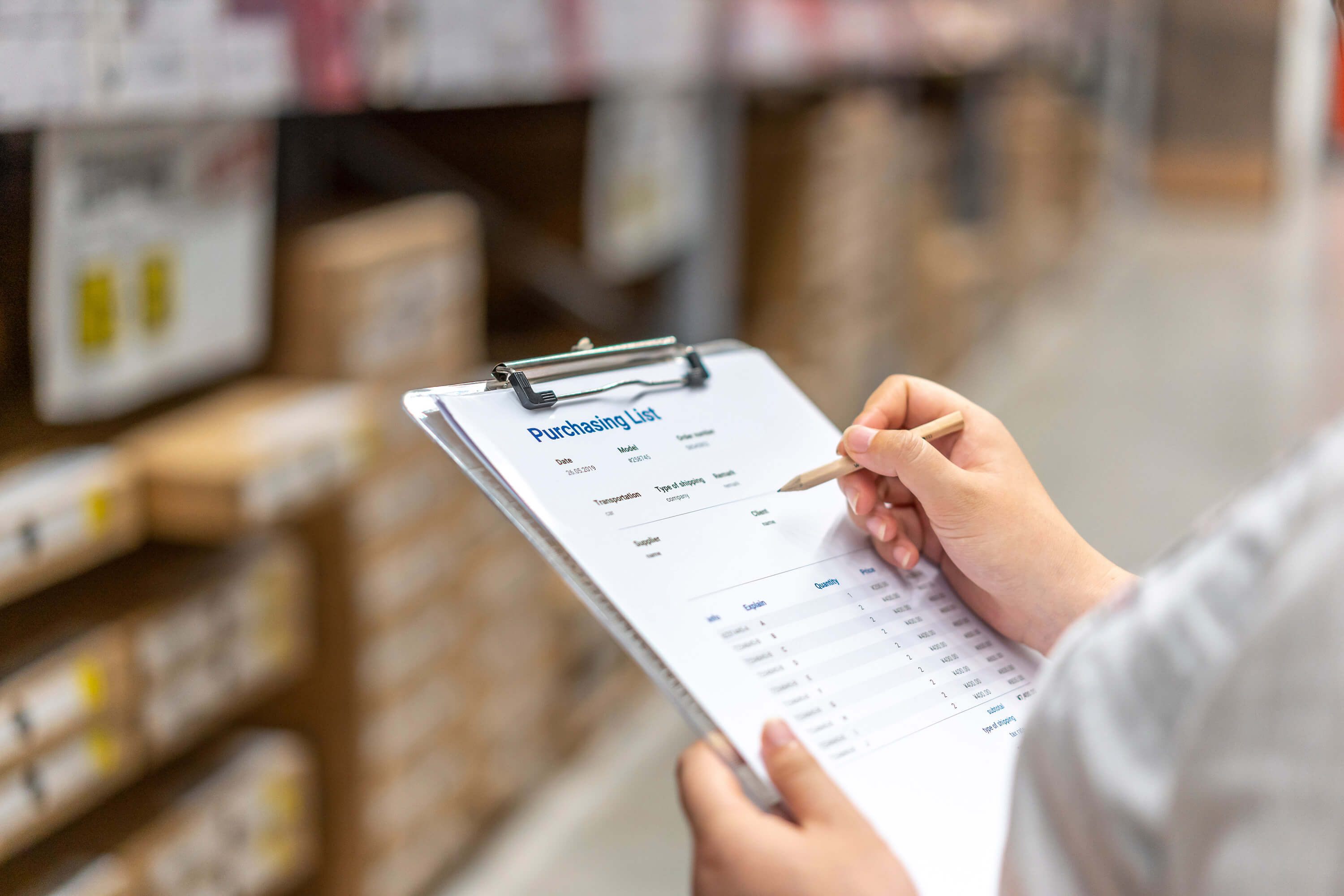 A woman in a warehouse holds a clipboard and pen.