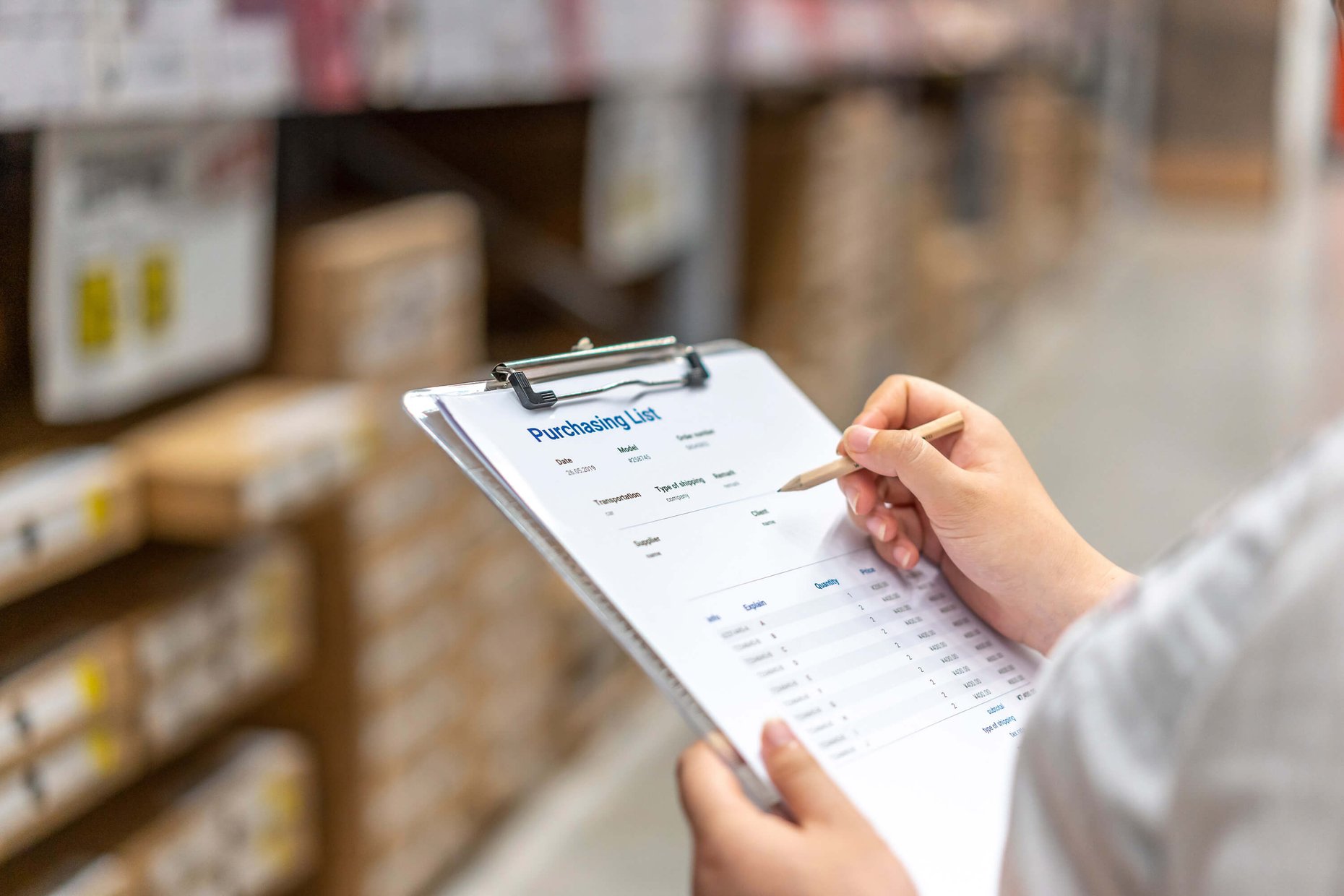 A woman in a warehouse holds a clipboard and pen.