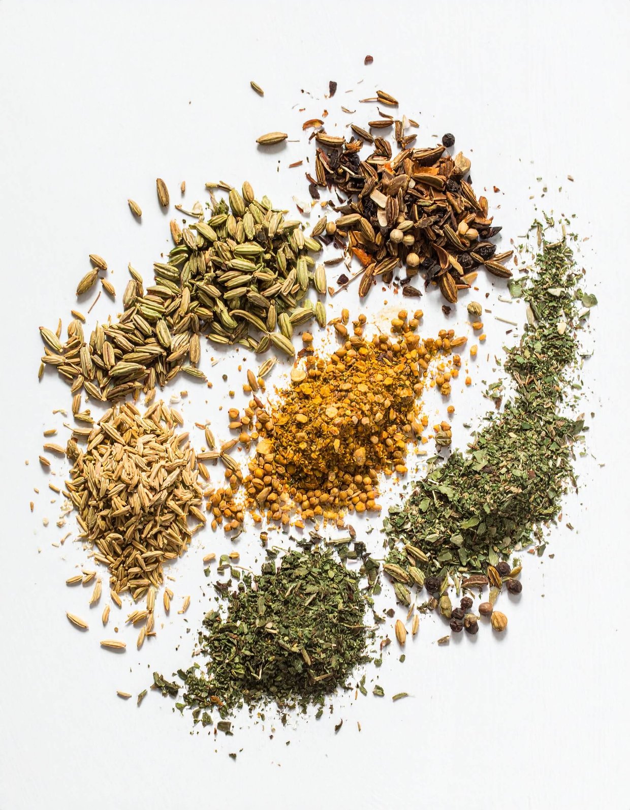 A variety of spices and herbs arranged on a white background, showcasing their colors and textures.