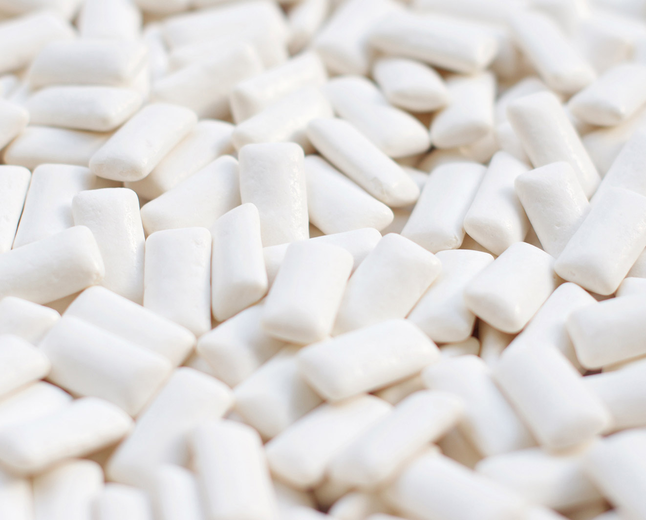 A close-up of a pile of white chewing gum, scattered on a flat surface.