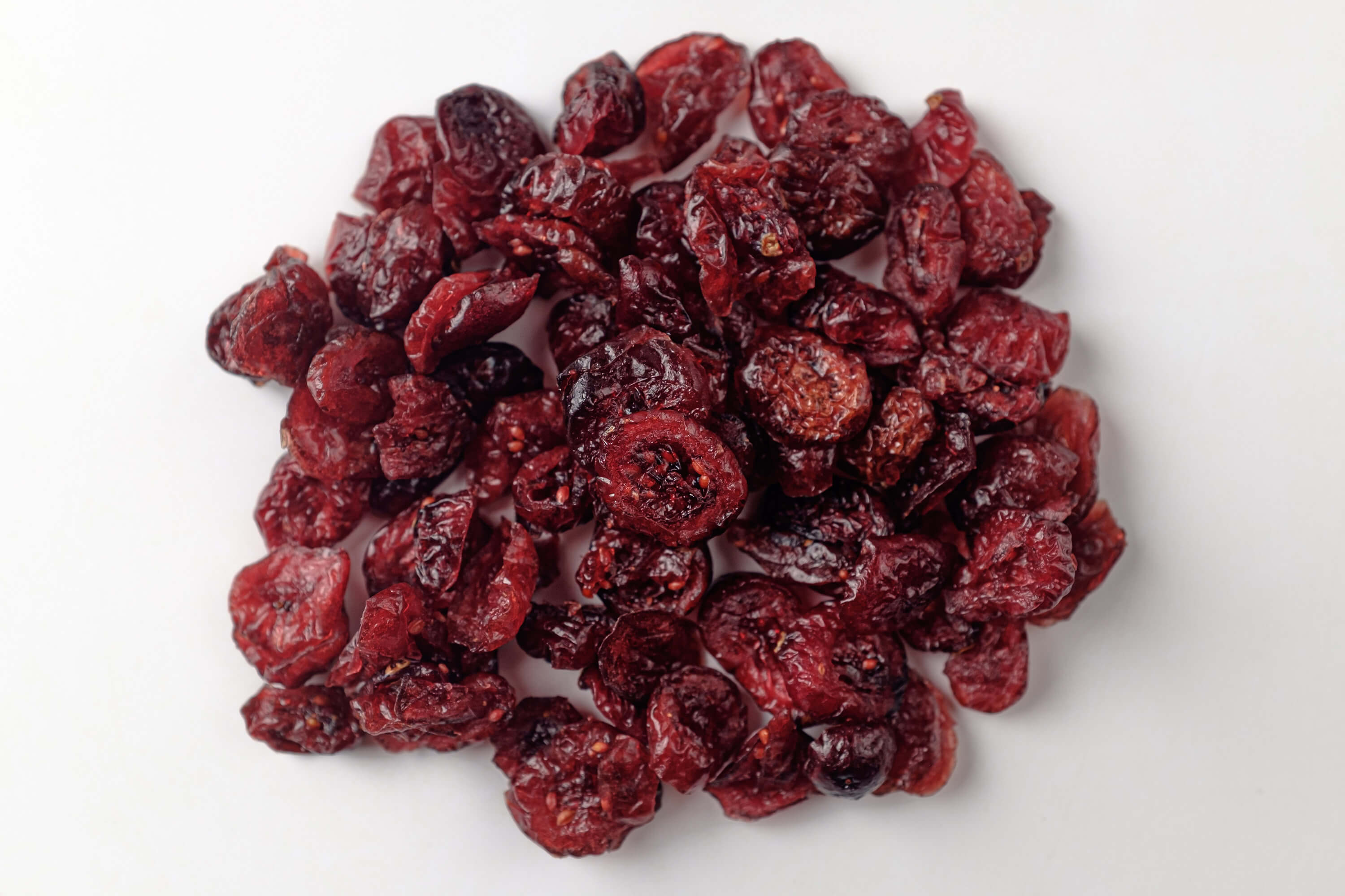 Dried cranberries scattered on a white background, showcasing their rich red color and wrinkled texture.