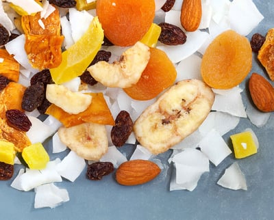 A vibrant pile of assorted dried fruits and nuts displayed on a blue background.