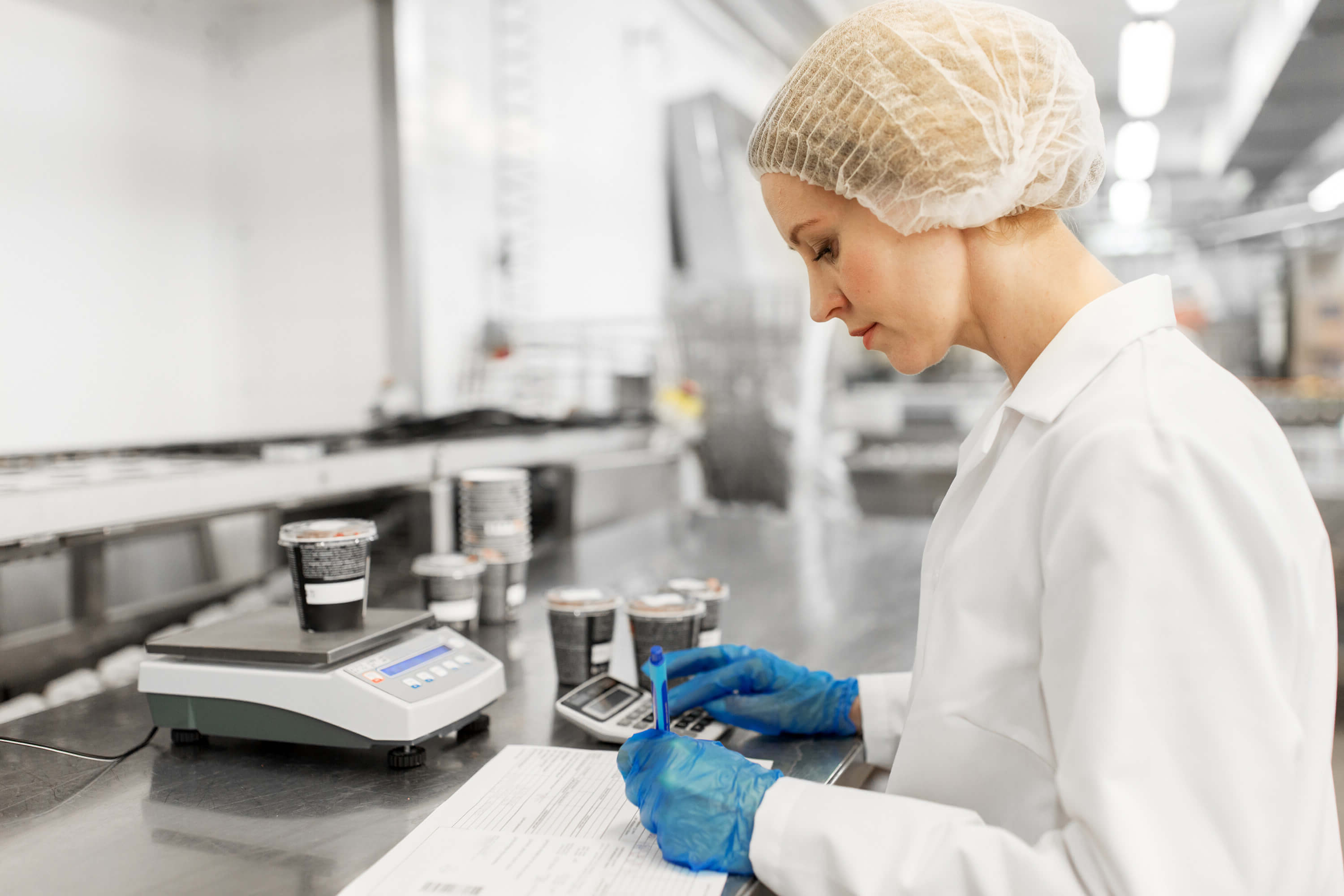 Food production worker recording measurements beside a precision scale in a clean processing facility.