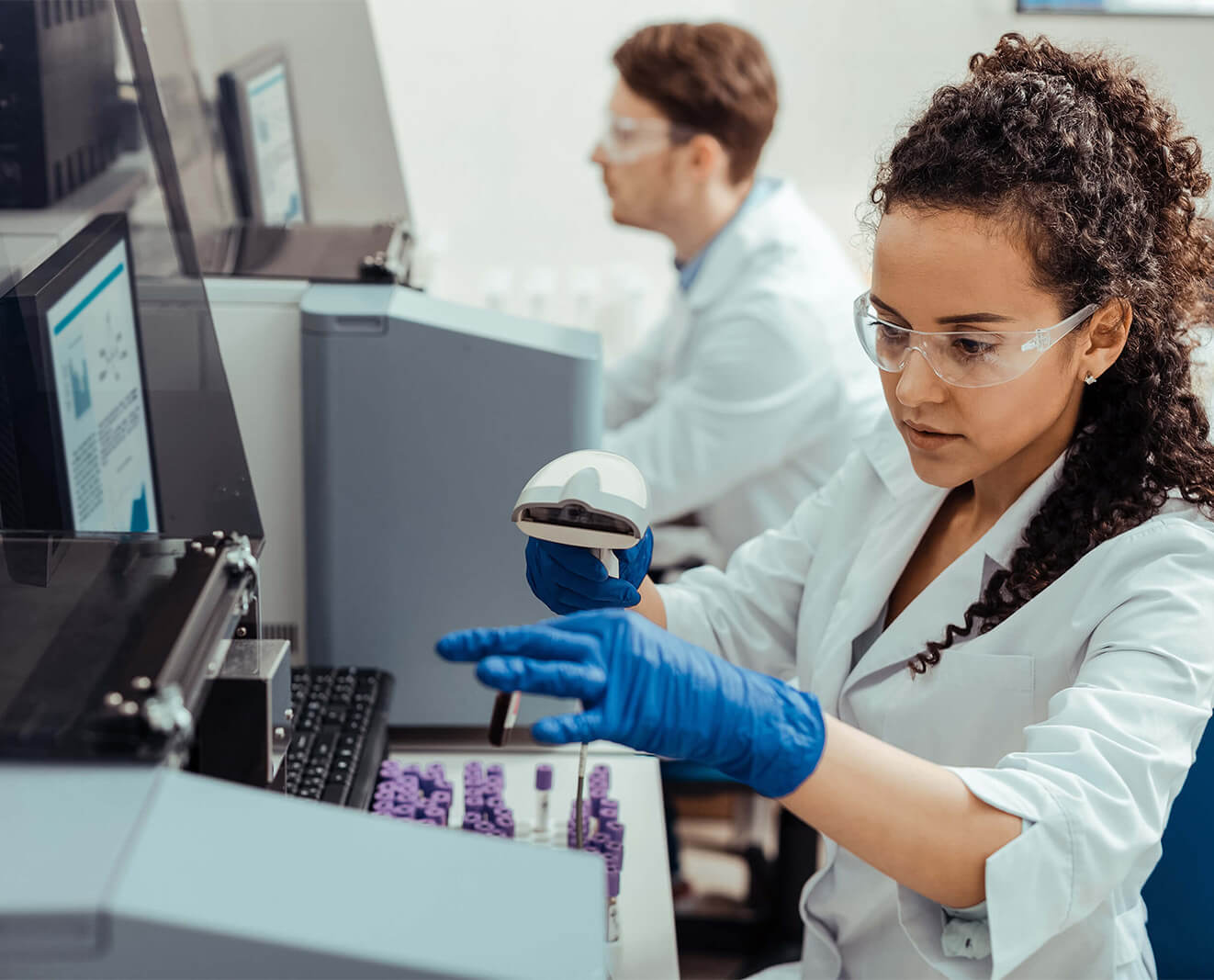 Lab technician in safety goggles handling a test tube in a clinical laboratory.