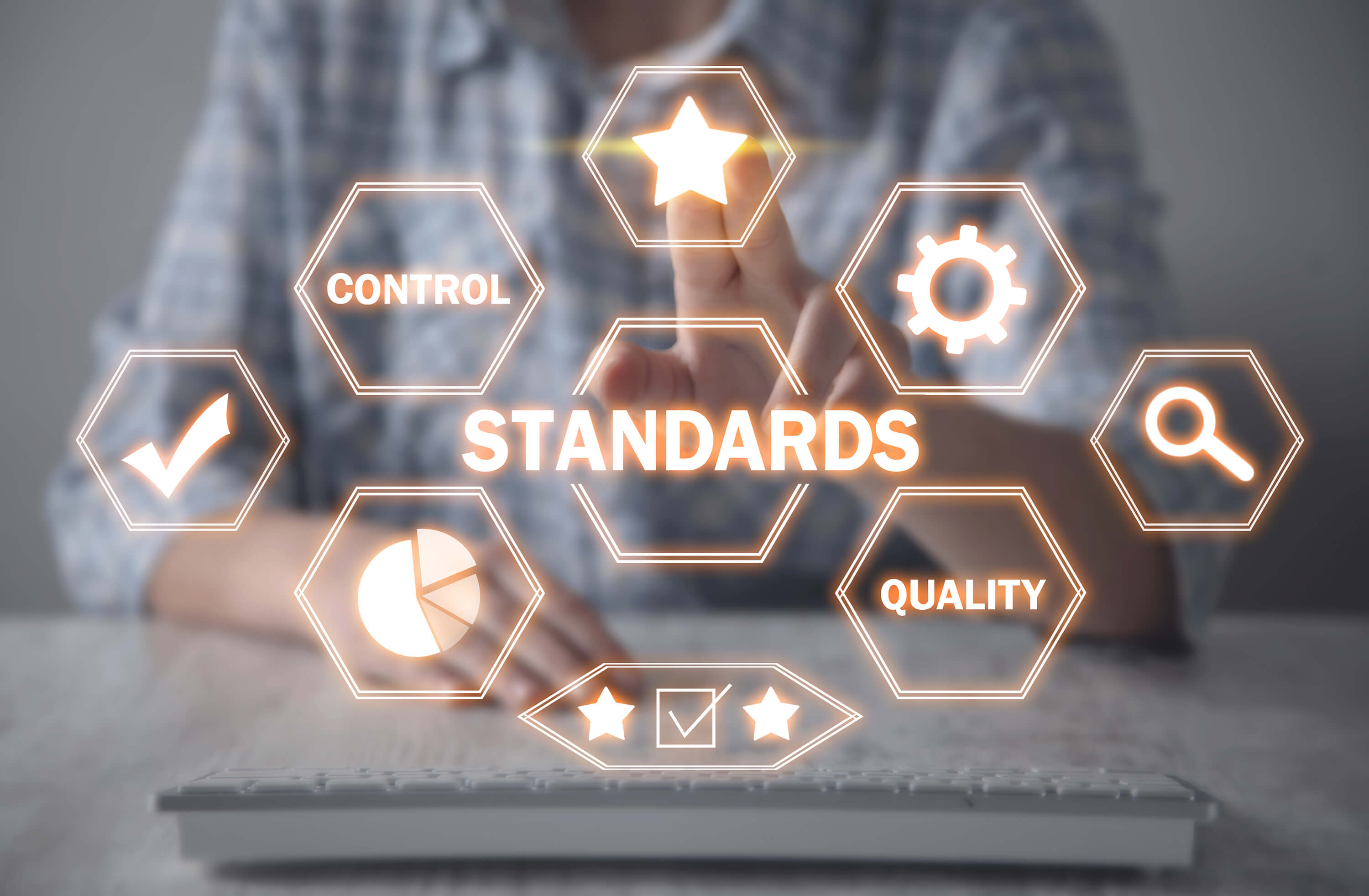 A person points toward quality and standards icons displayed above a keyboard.