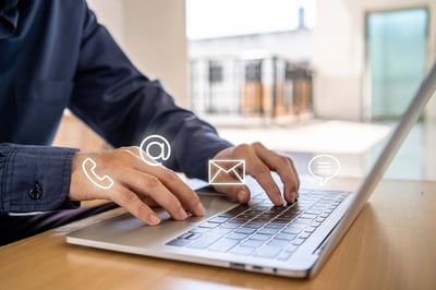 Person typing on a laptop with digital communication icons for phone, email, and chat.