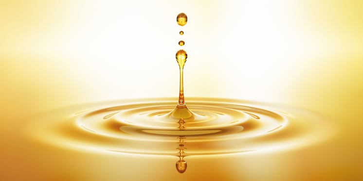 A glossy oil drop is positioned against a vivid yellow background, emphasizing its shape and reflective qualities.