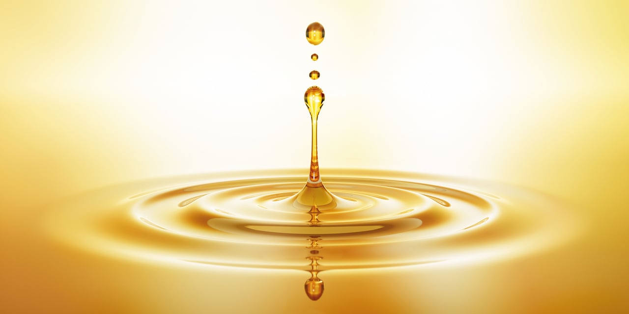 A glossy oil drop is positioned against a vivid yellow background, emphasizing its shape and reflective qualities.