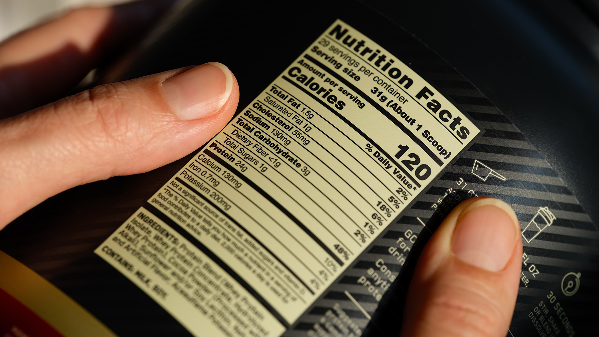 Close-up of black jar of whey protein powder with nutrition facts label in scientists Hands.