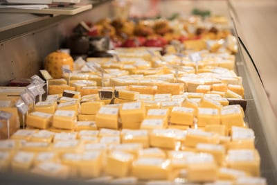 Various packaged cheese blocks displayed in a refrigerated supermarket counter.