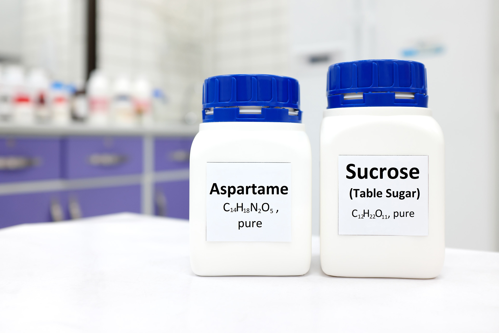 Selective focus of a bottle of pure aspartame artificial sweetener and sucrose or table sugar chemical compound comparison.