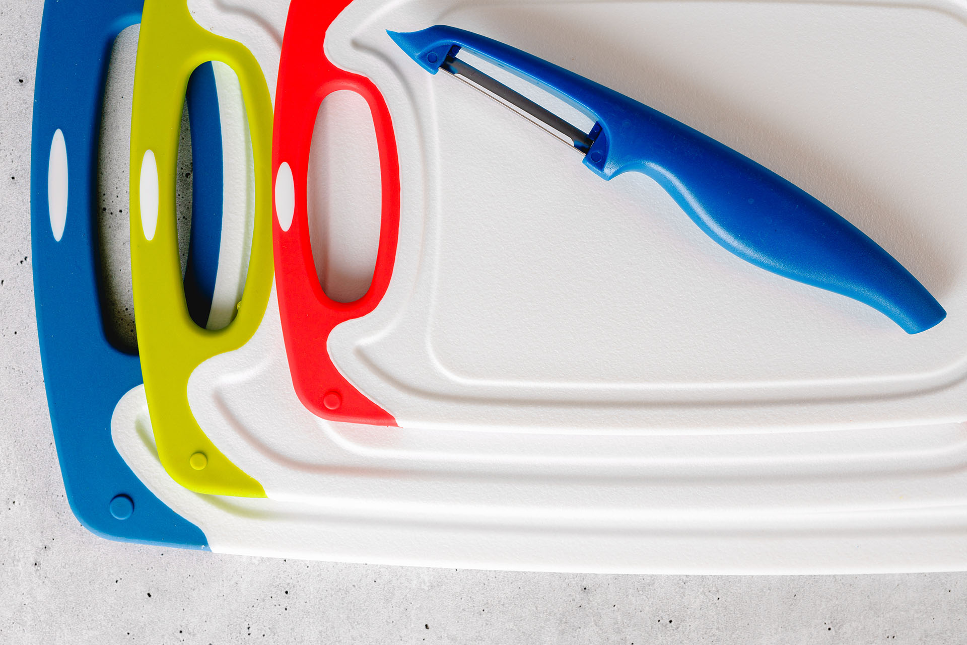Plastic cutting boards and a peeler arranged on a light surface.
