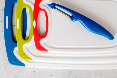 Plastic cutting boards and a peeler arranged on a light surface.