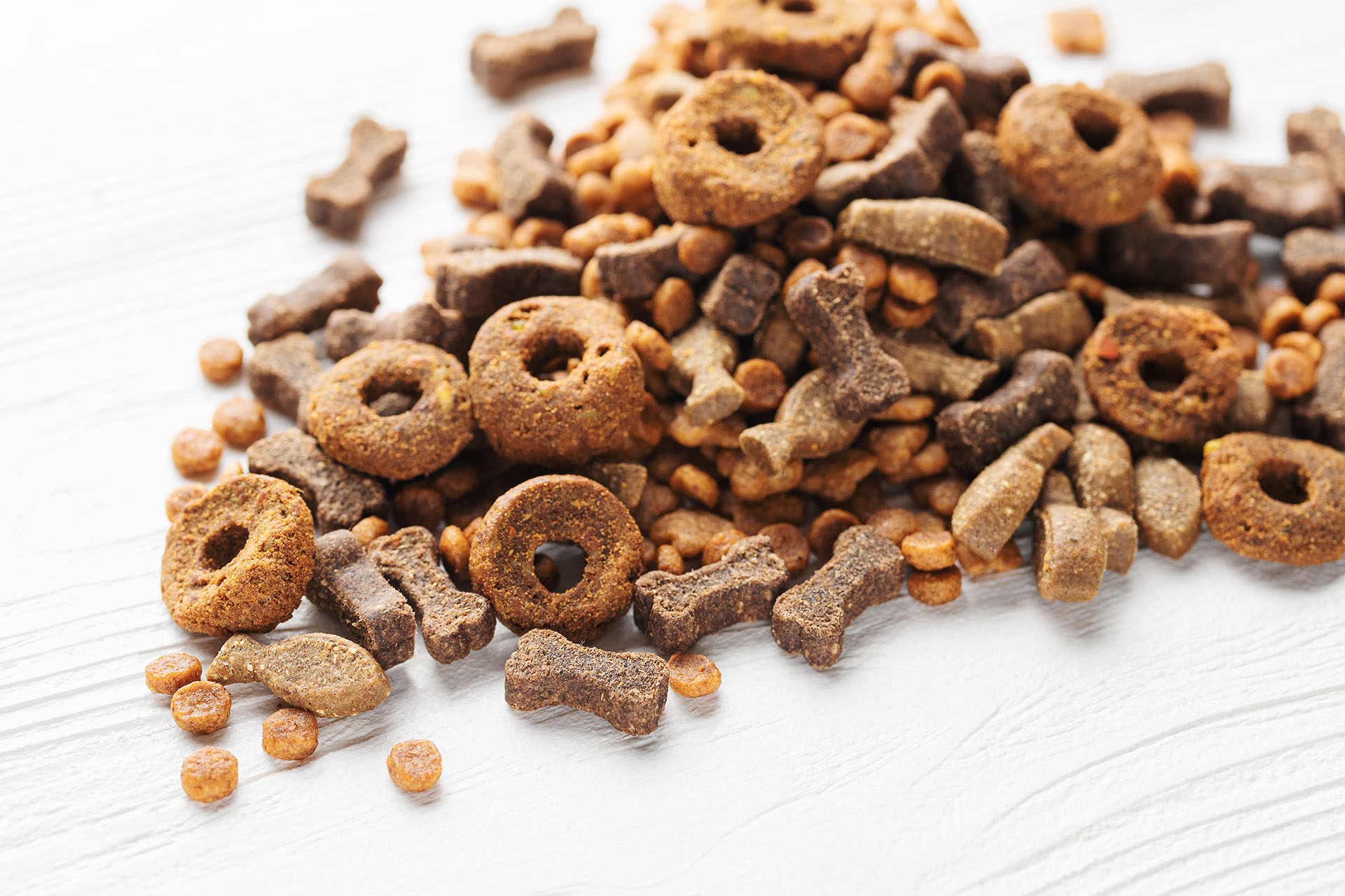Dry nutrition food for dogs of different shapes on a white wooden background.