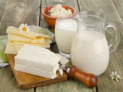 Milk jug and glass with assorted cheeses and curd on a wooden table._@bit24