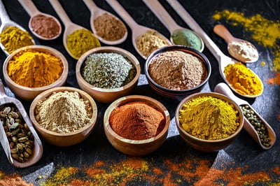 Assorted ground spices in wooden bowls and spoons arranged on a dark surface.
