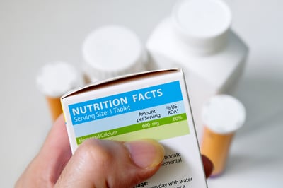 Hand examining a nutrition facts label on supplement packaging to assess nutritional information.